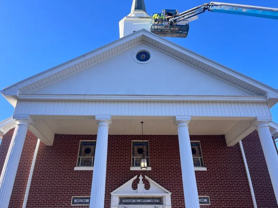Roofing crew repairing the steeple of a local church using a lift
