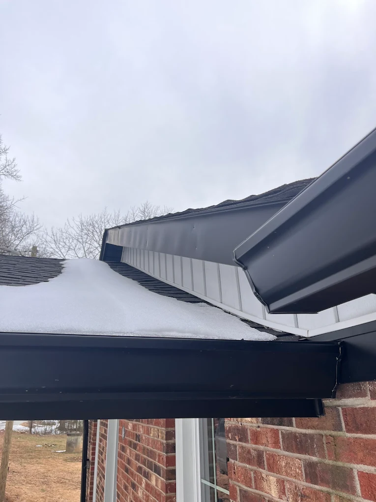 New black seamless gutters installed along the roofline of a brick home