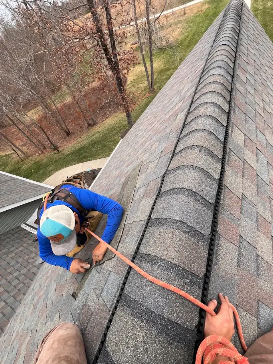Roofer installing ridge cap shingles along a roofline